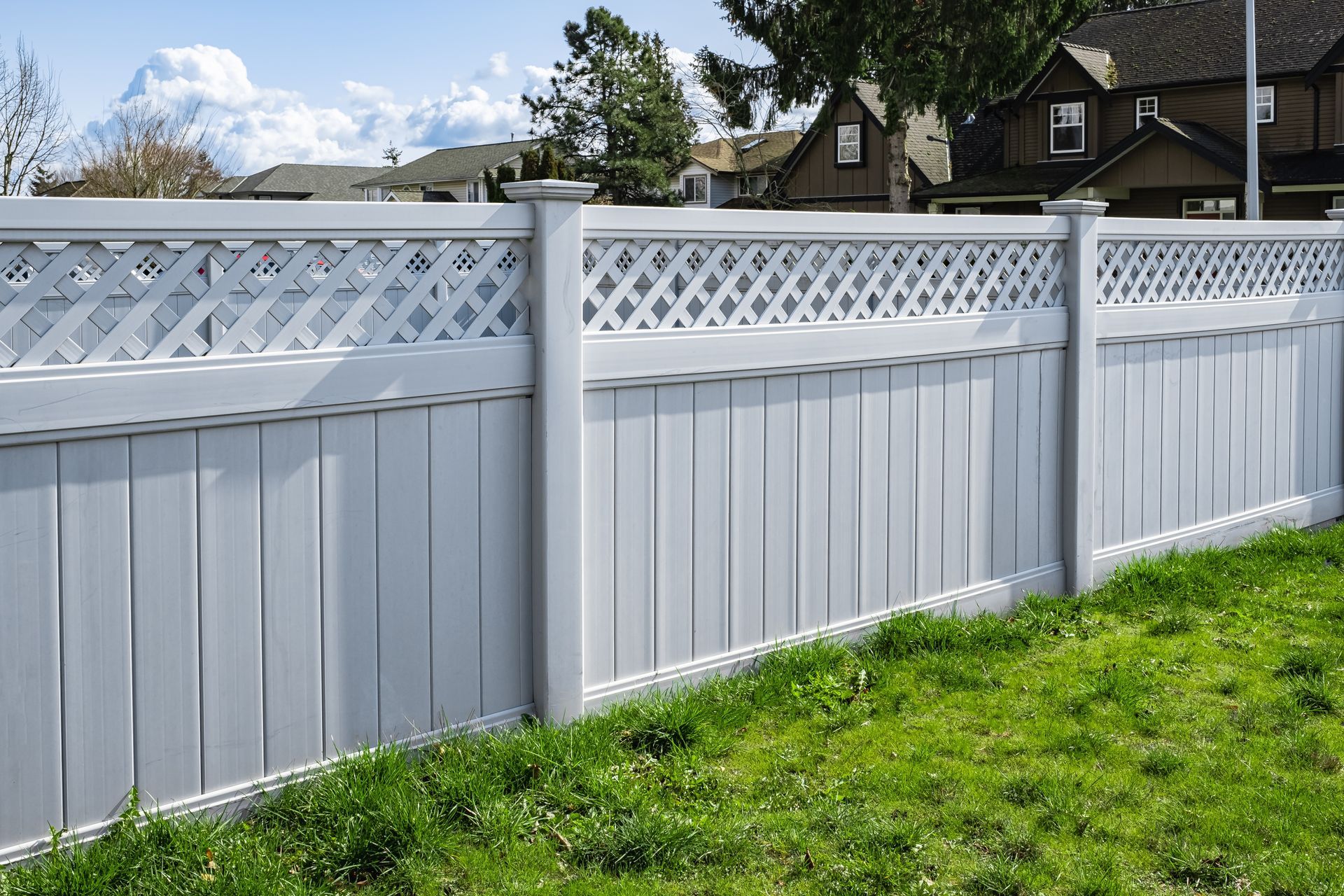 White vinyl fence with lattice top beside a green lawn in a suburban yard