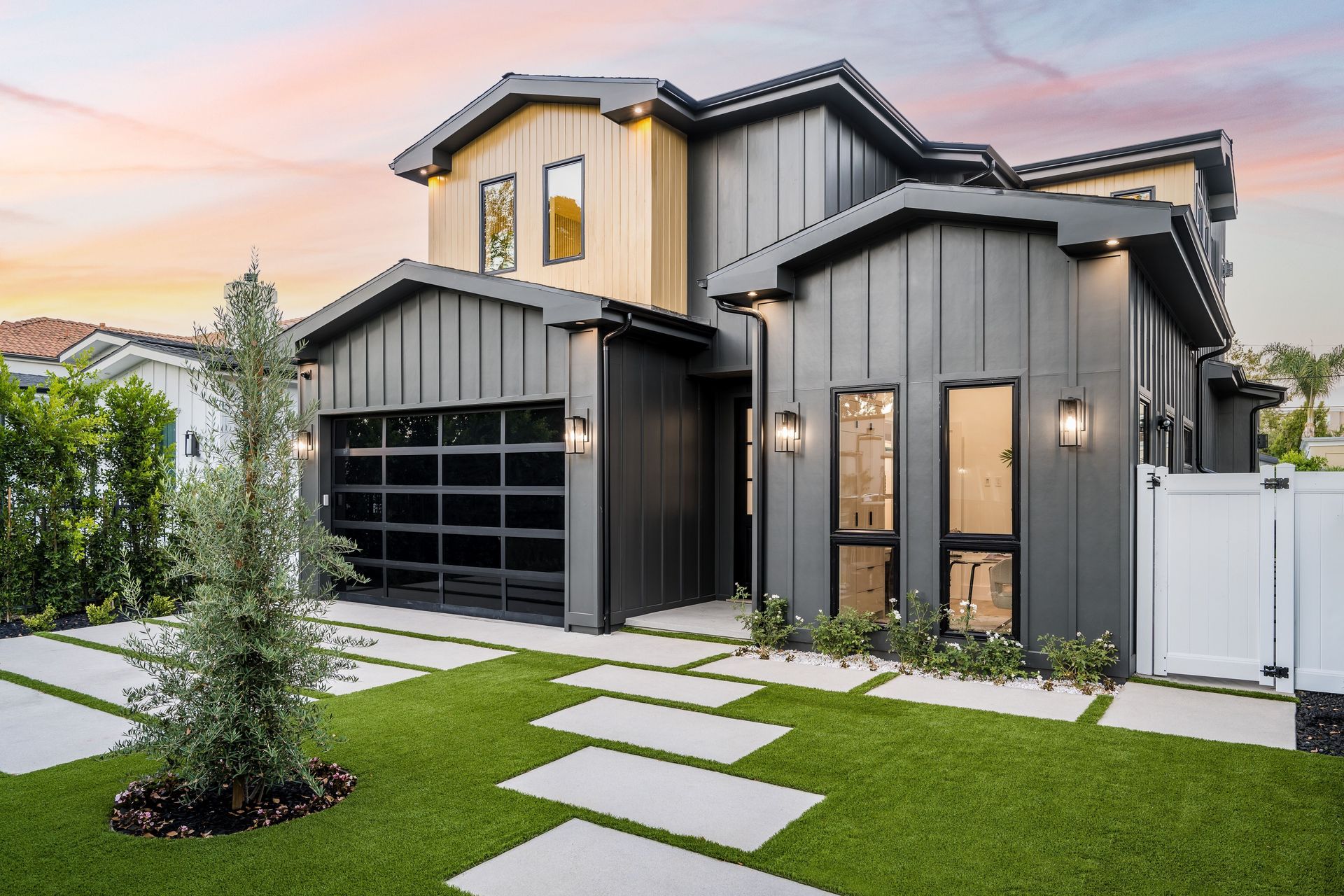 Modern two-story house with dark gray siding, black garage door, and a walkway over green grass.