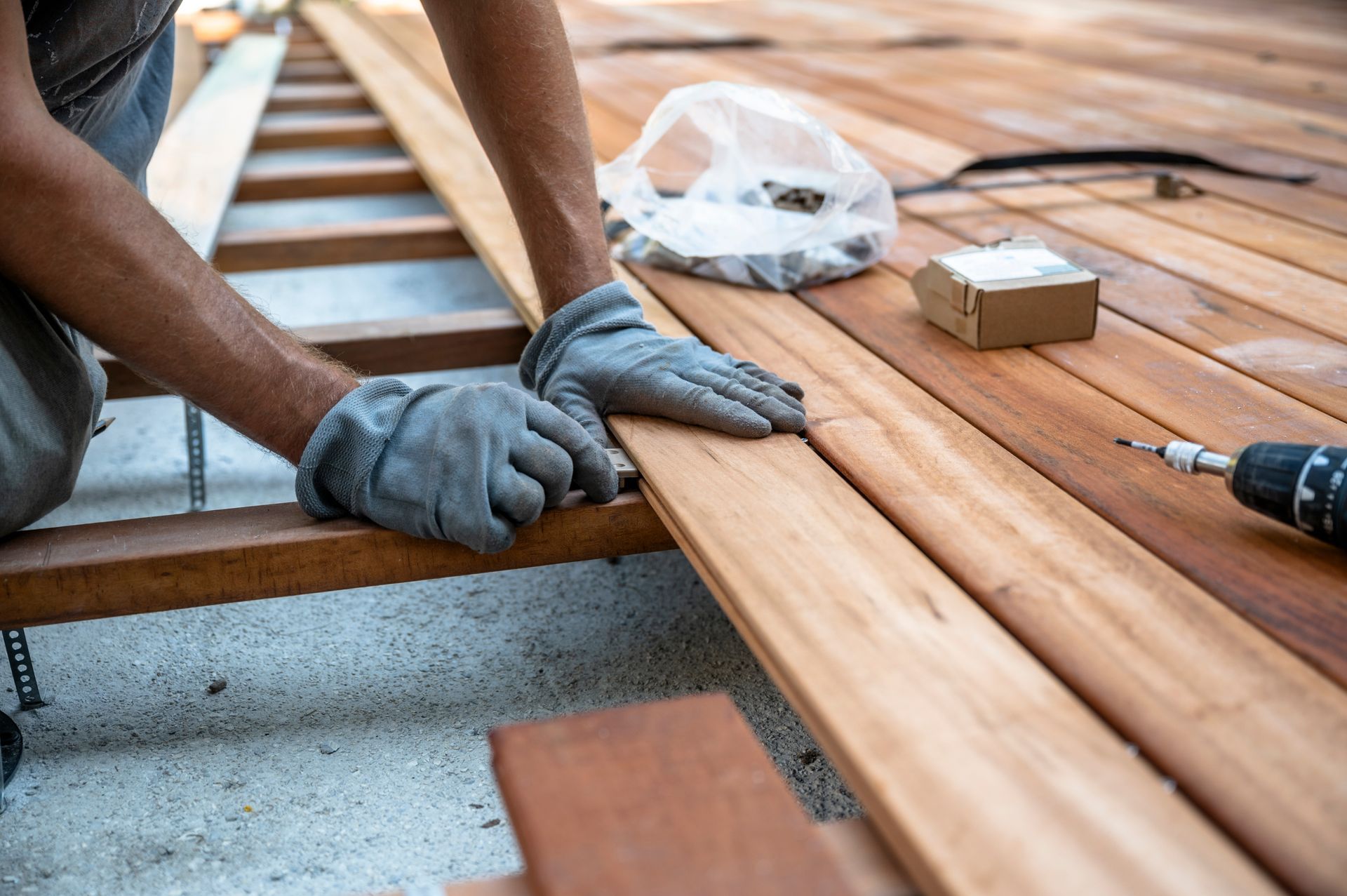 Person wearing gloves installing wooden deck boards with a drill and screws.