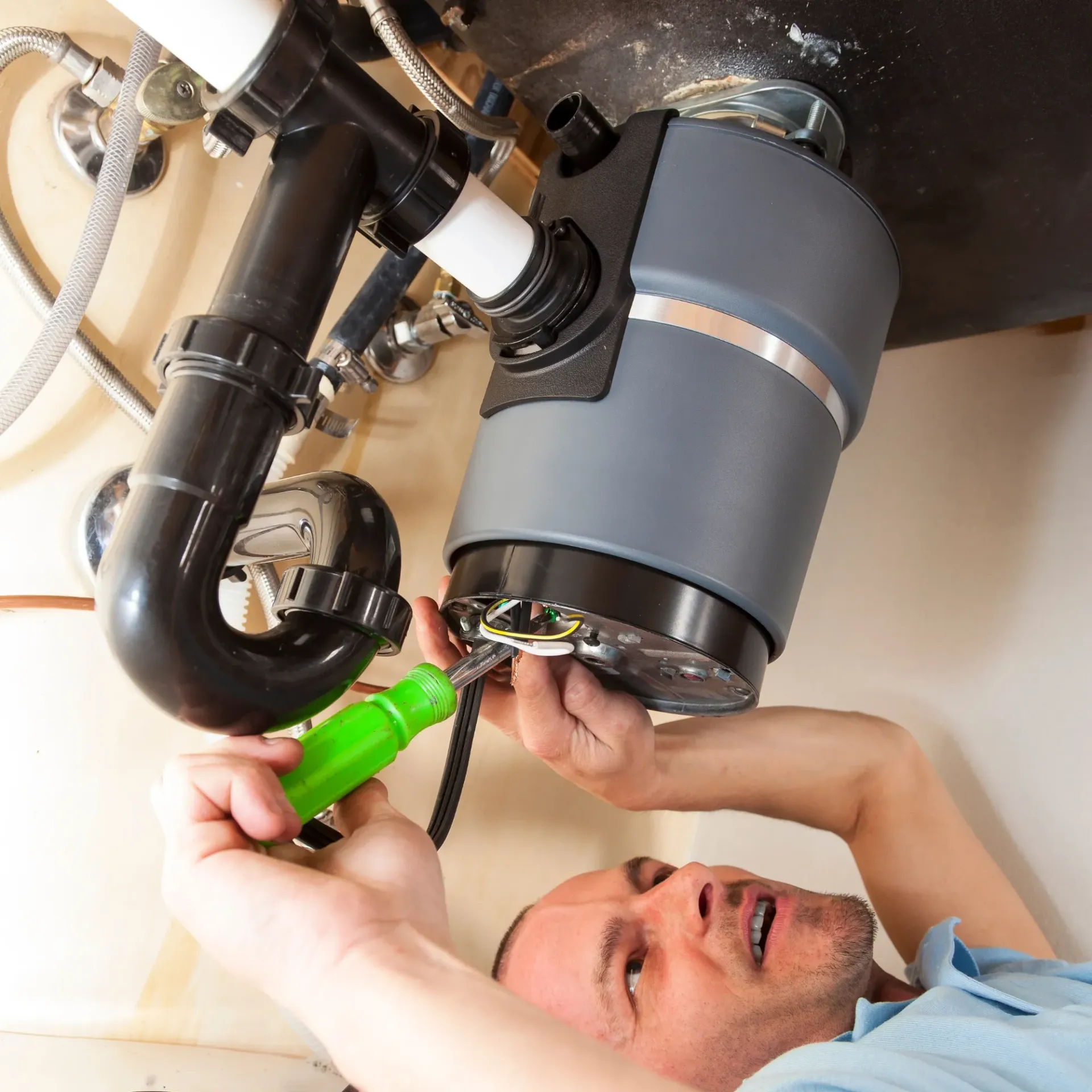 Ted & Bros Plumbing | man is fixing a garbage disposal with a green screwdriver