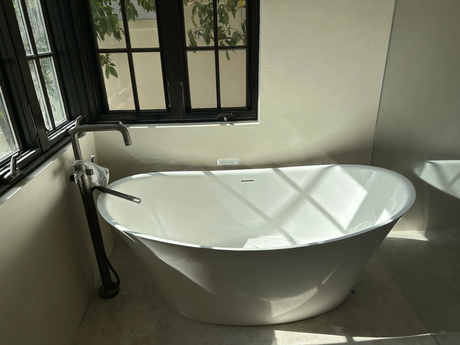 Ted & Bros Plumbing | person wearing black gloves is holding a faucet in front of a bathtub.