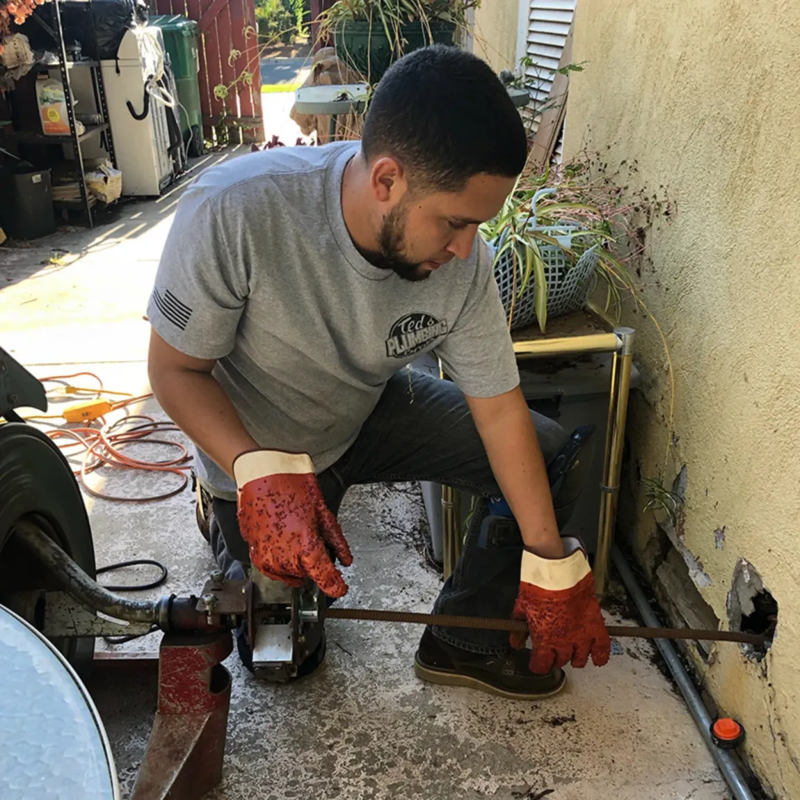 Ted & Bros Plumbing | man wearing red gloves is working on a pipe.