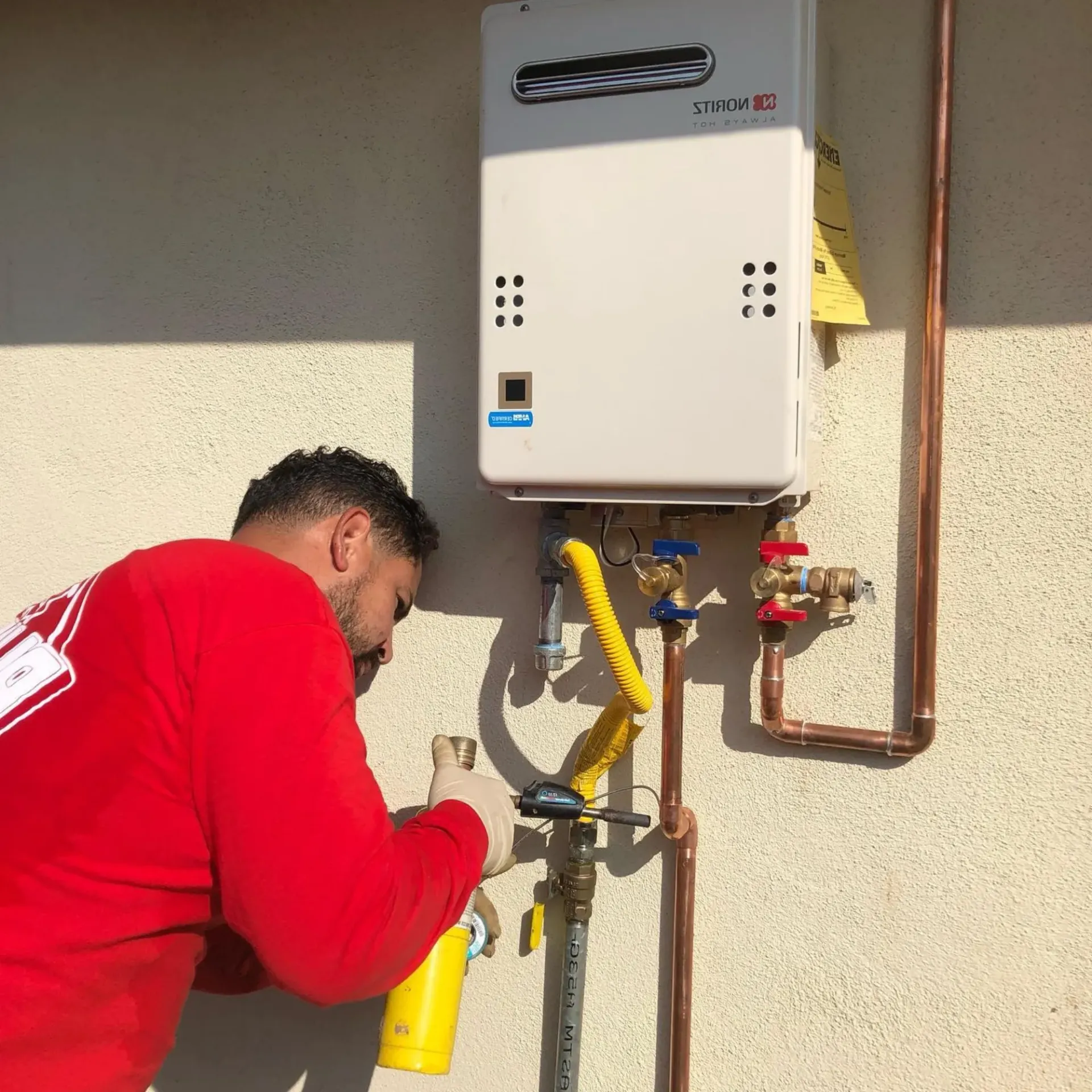Ted & Bros Plumbing | man in a red shirt is working on a water heater