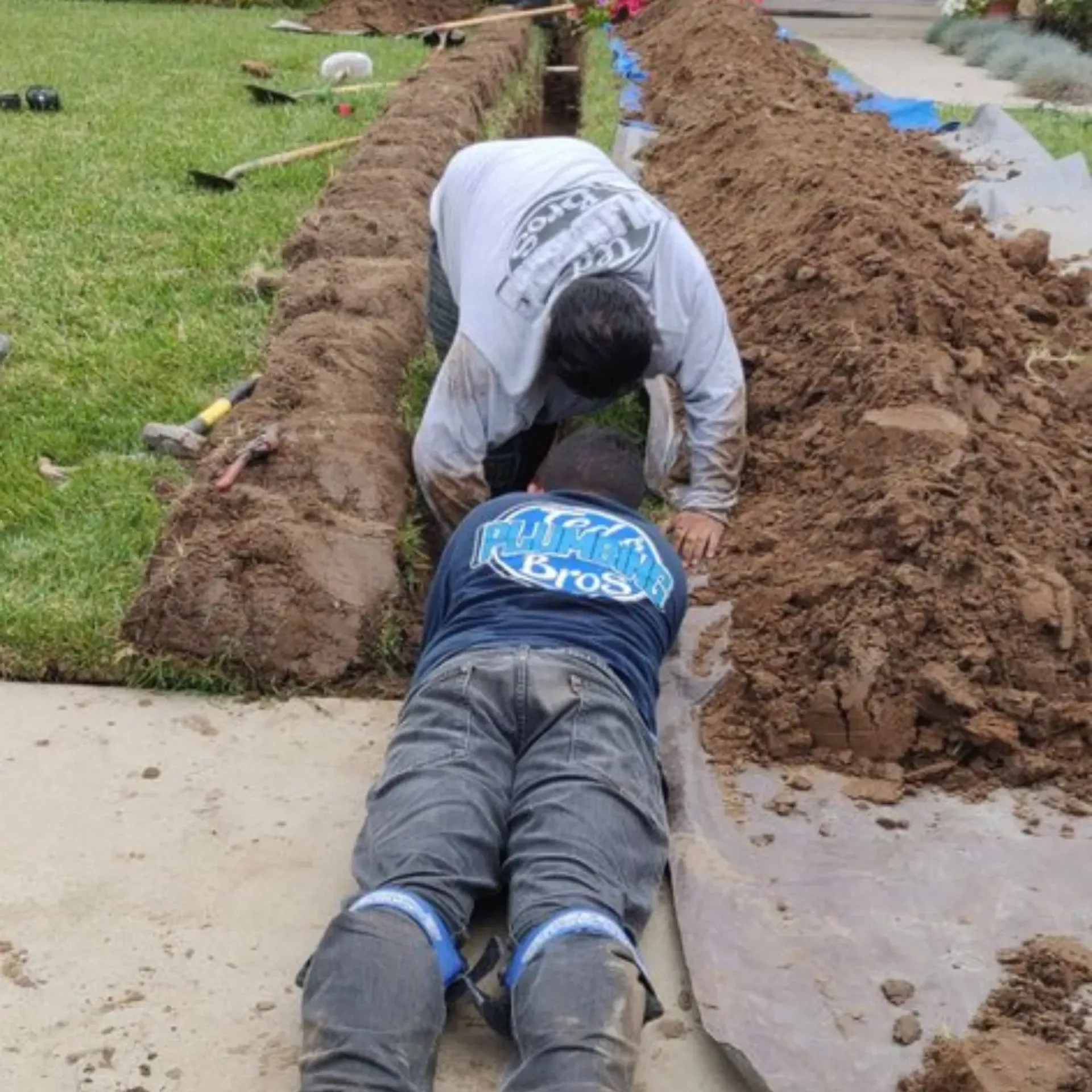 Ted & Bros Plumbing | Two men are working on a drainage system in a yard.