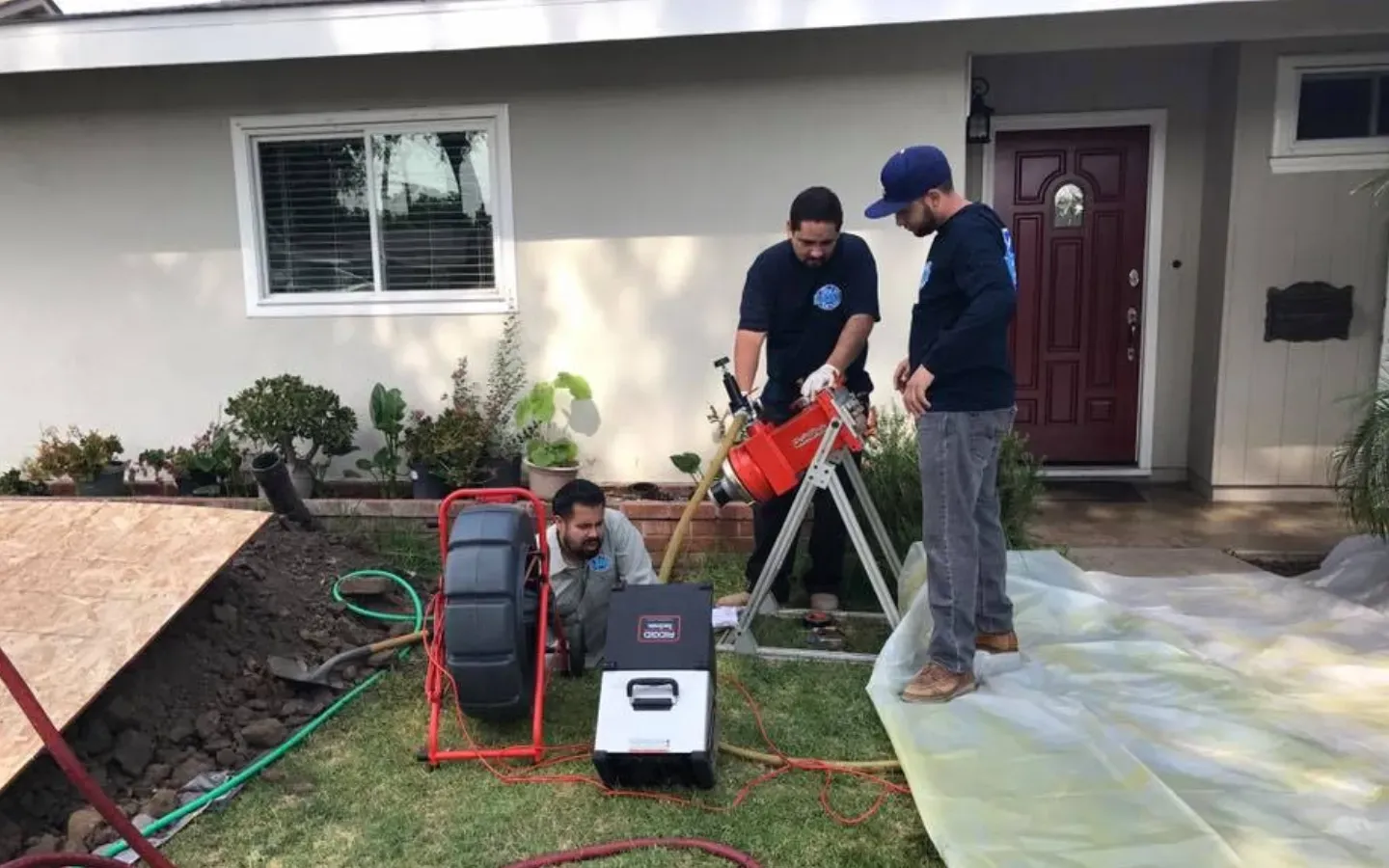 Ted & Bros Plumbing | group of men are working on a drain in front of a house.