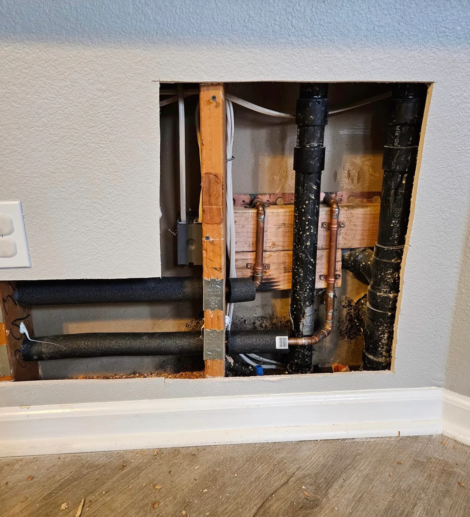 Ted & Bros Plumbing | man in overalls is fixing a pipe on a wall