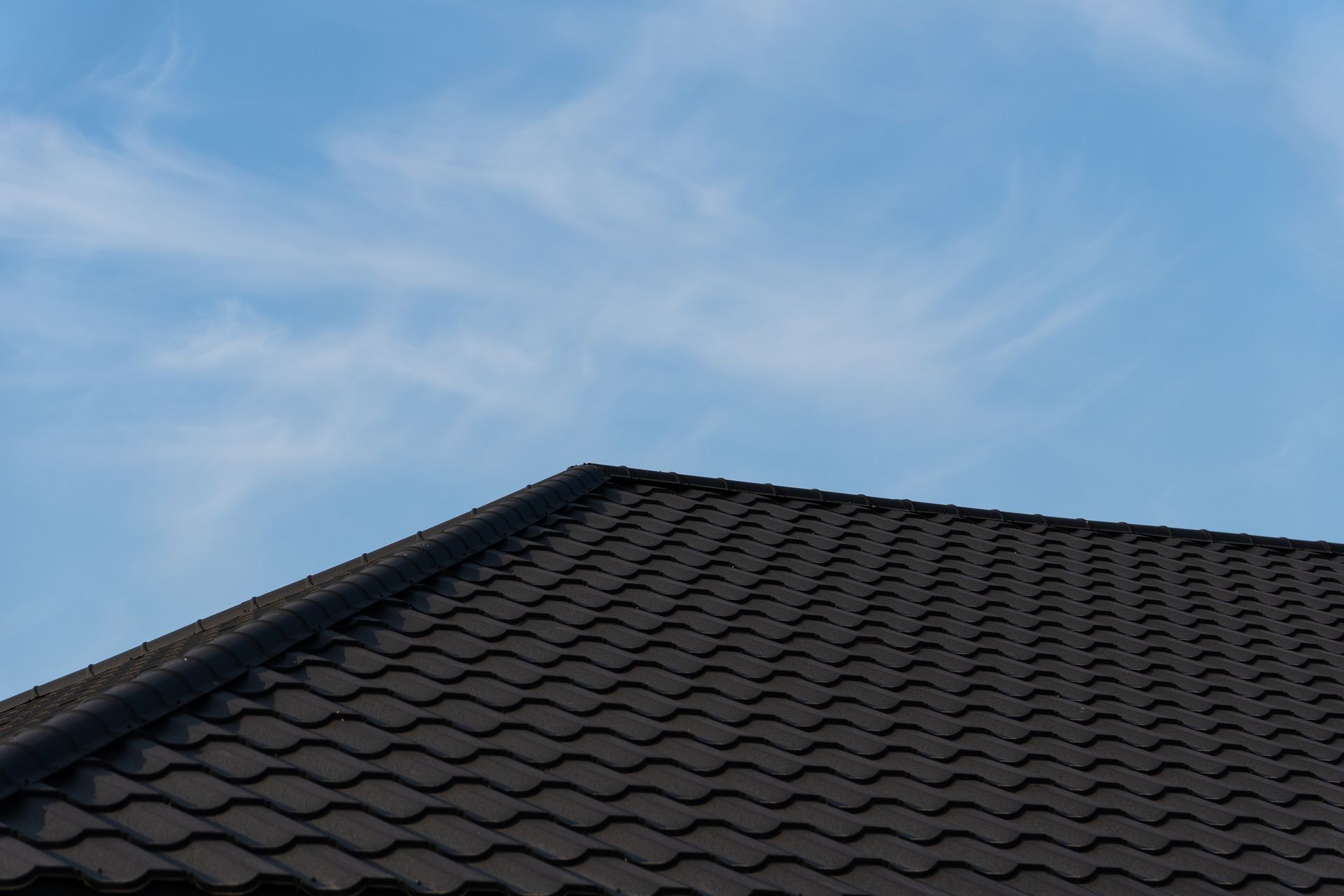 Dark tiled roof against a blue sky with wispy clouds