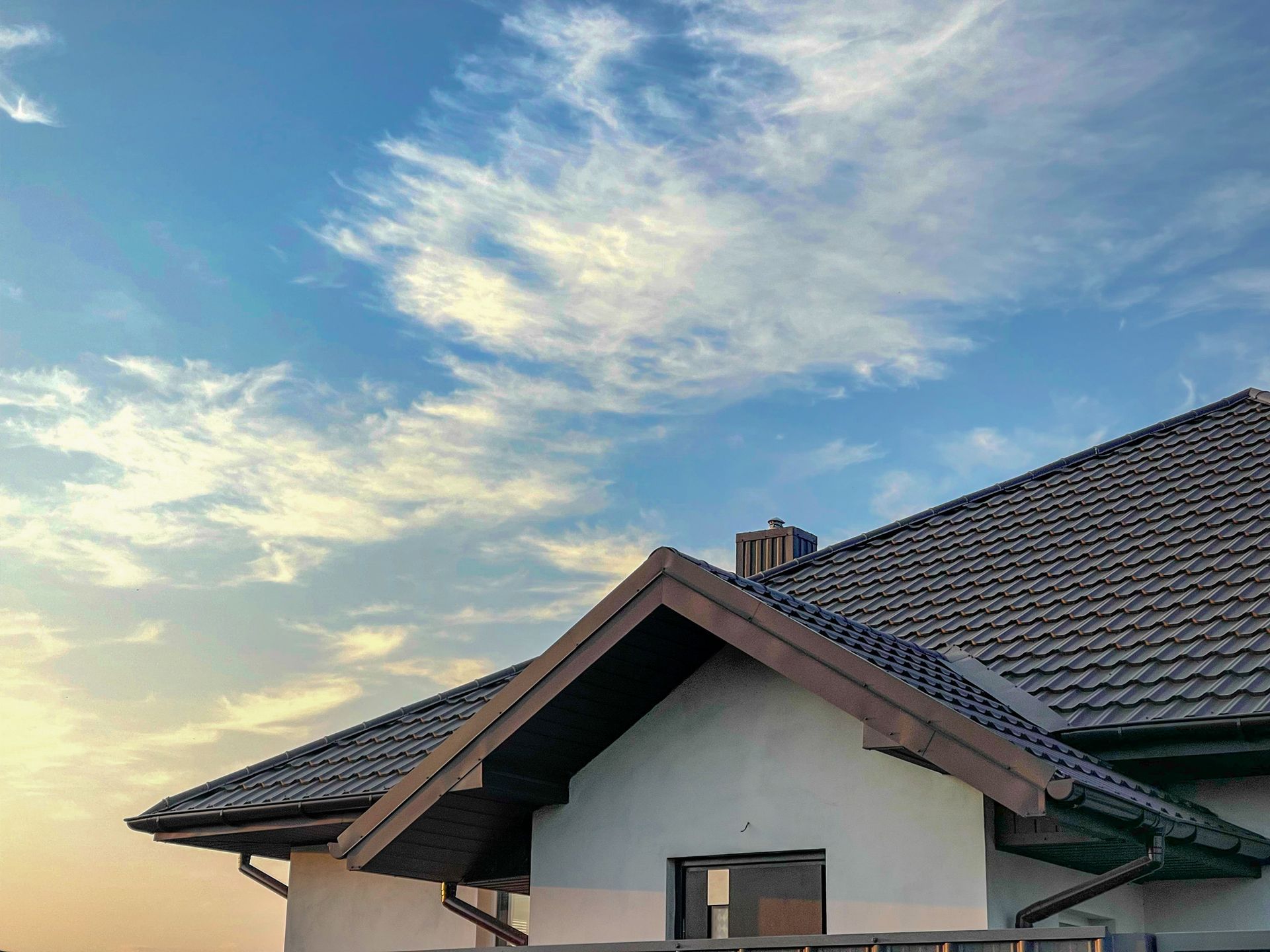 House roof beneath a partly cloudy blue sky at sunset