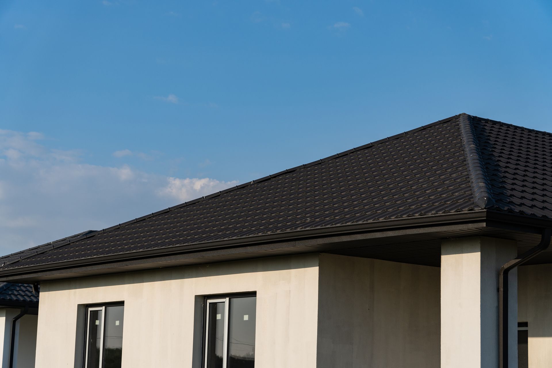 Modern house roof with dark shingles under a blue sky