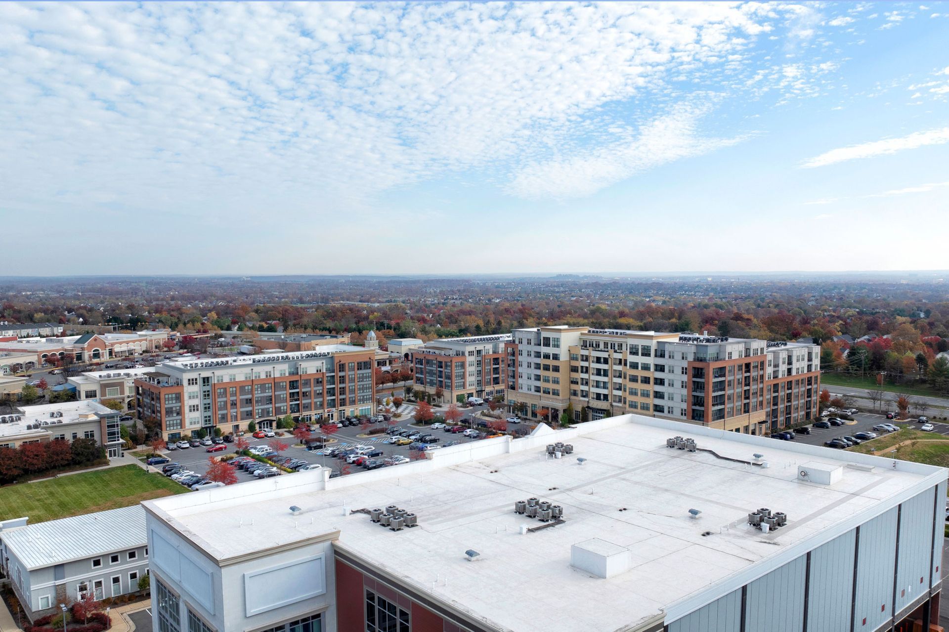 Aerial view of apartment buildings and a white rooftop under a blue, cloud-streaked sky.