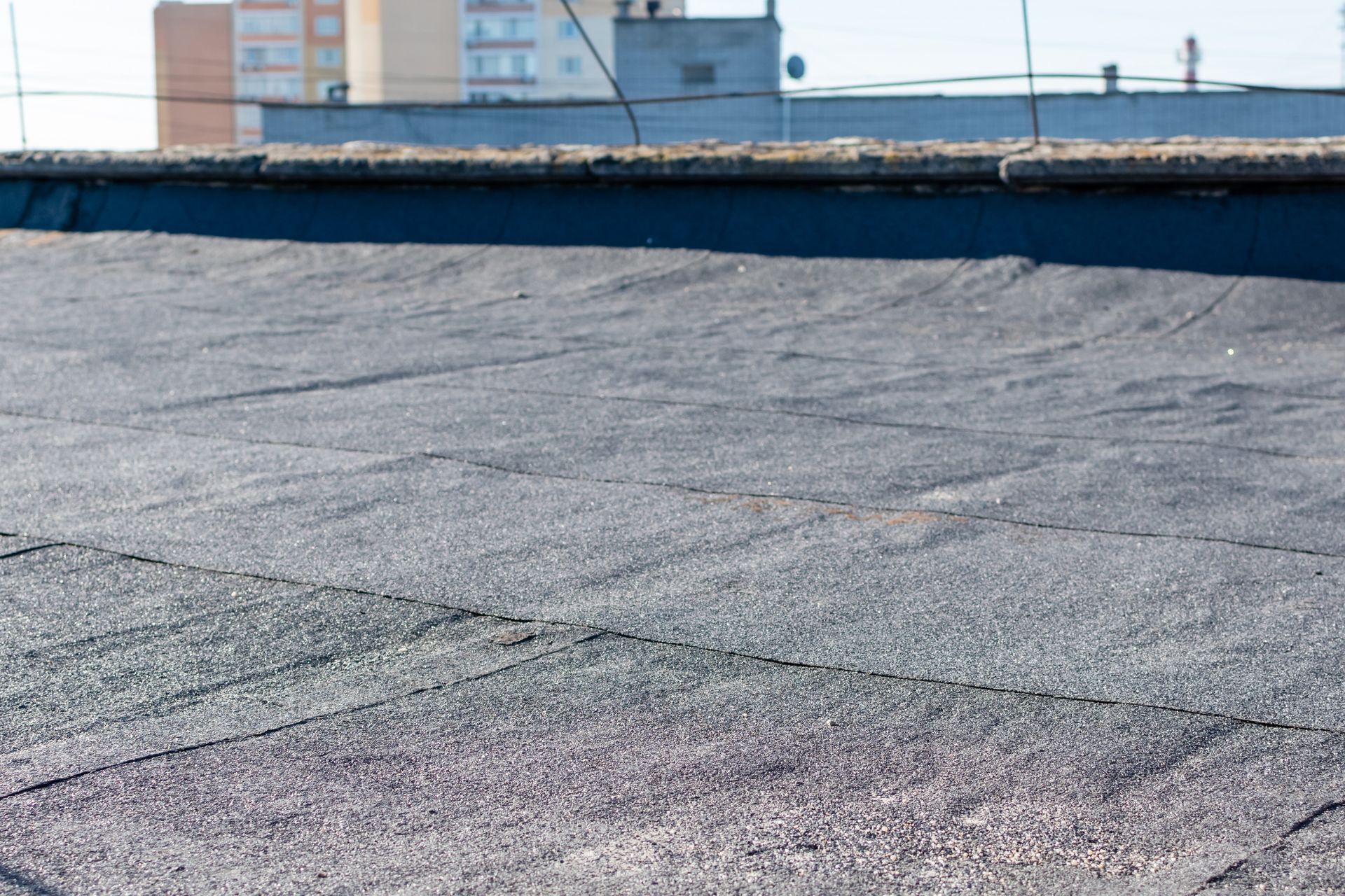 Flat gravel rooftop with a low blue parapet wall and distant industrial building in bright daylight
