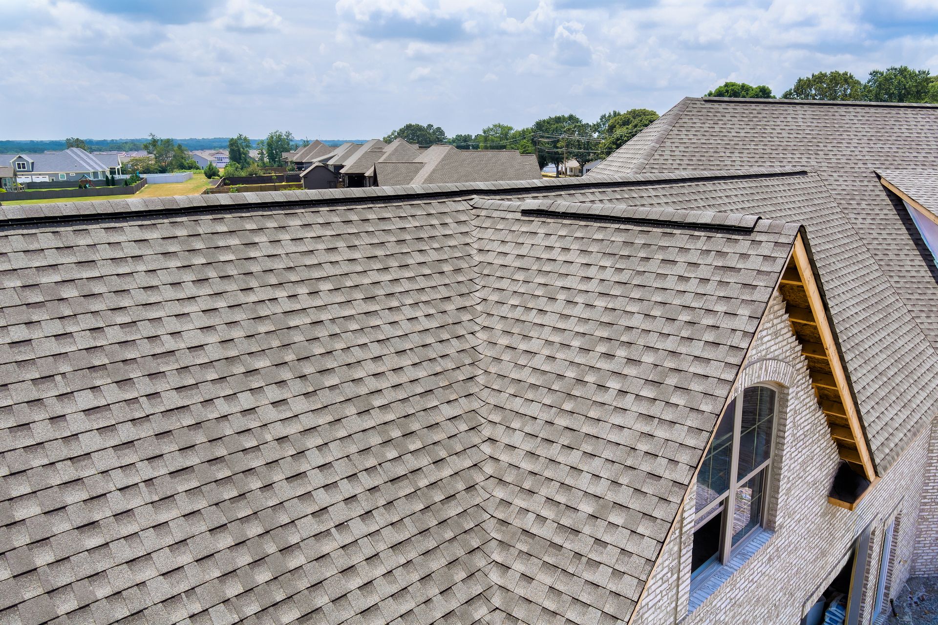 Aerial view of gray shingled rooftops on houses under a partly cloudy sky