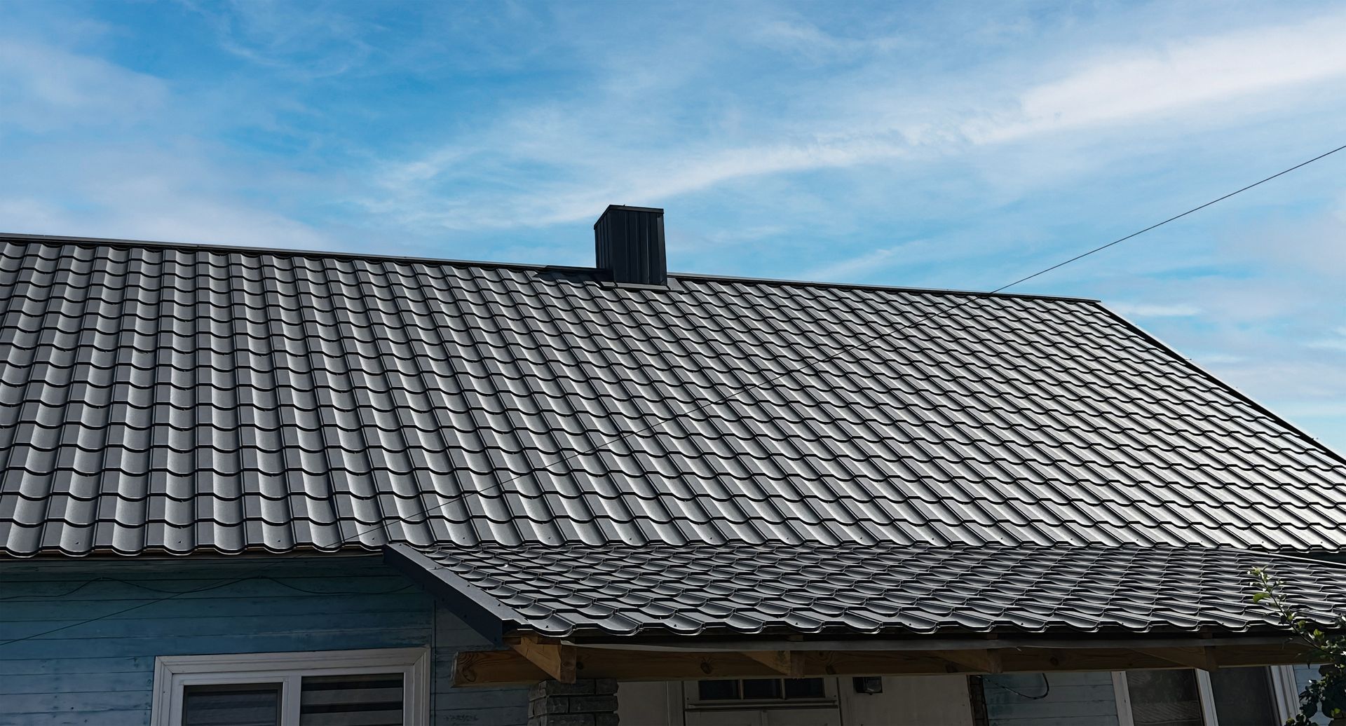 Gray tiled roof with a small chimney under a blue sky.