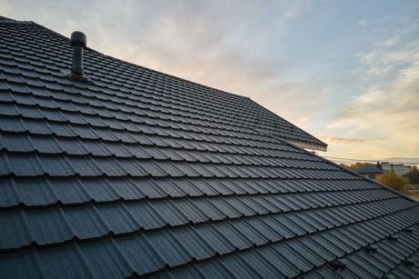 Slate roof tiles at sunset with a metal vent pipe against a cloudy sky