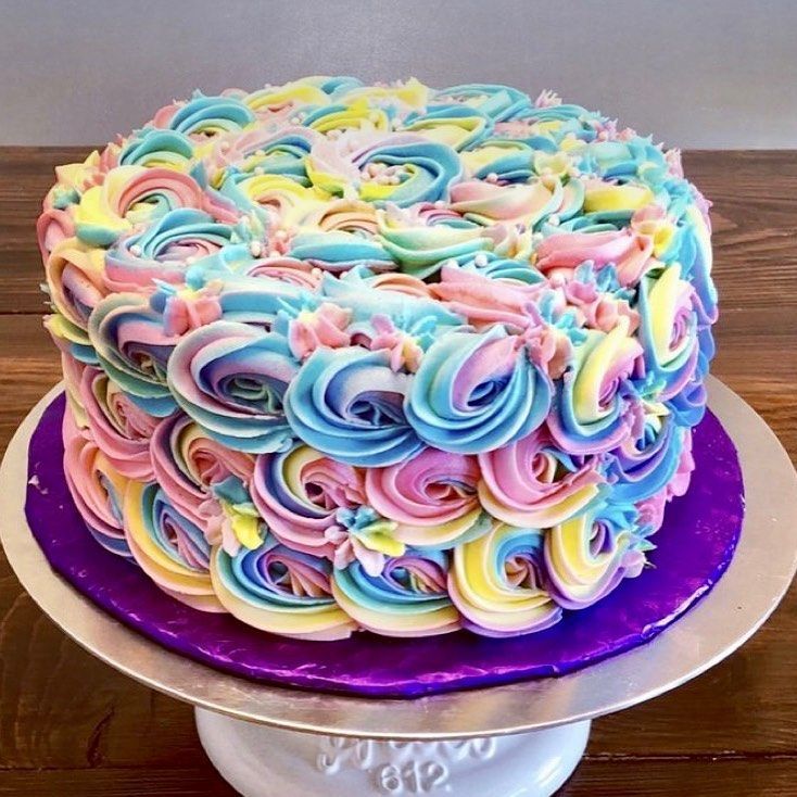 Colorful pastel rosette cake on a silver stand with a purple board