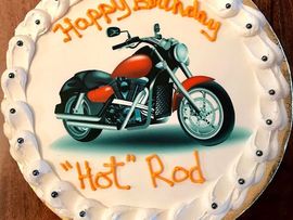 Motorcycle-themed birthday cake with orange “Happy Birthday” and “Hot Rod” icing