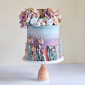 Pastel-frosted cake with floral top and tiny figurines on a cake stand