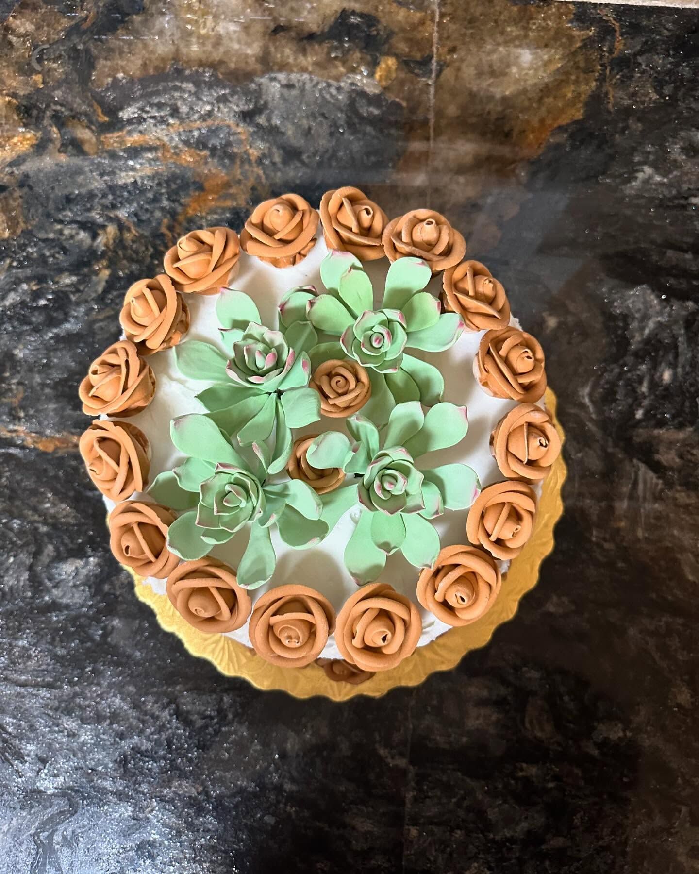 Round dessert topped with tan and mint-green frosting roses on a dark surface