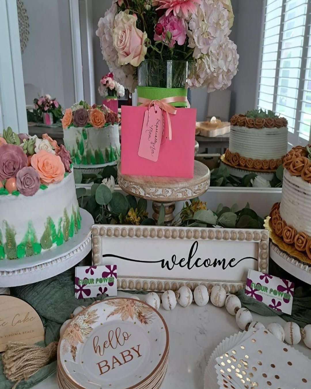 Baby shower dessert table with pastel cakes, flowers, and a “welcome” sign