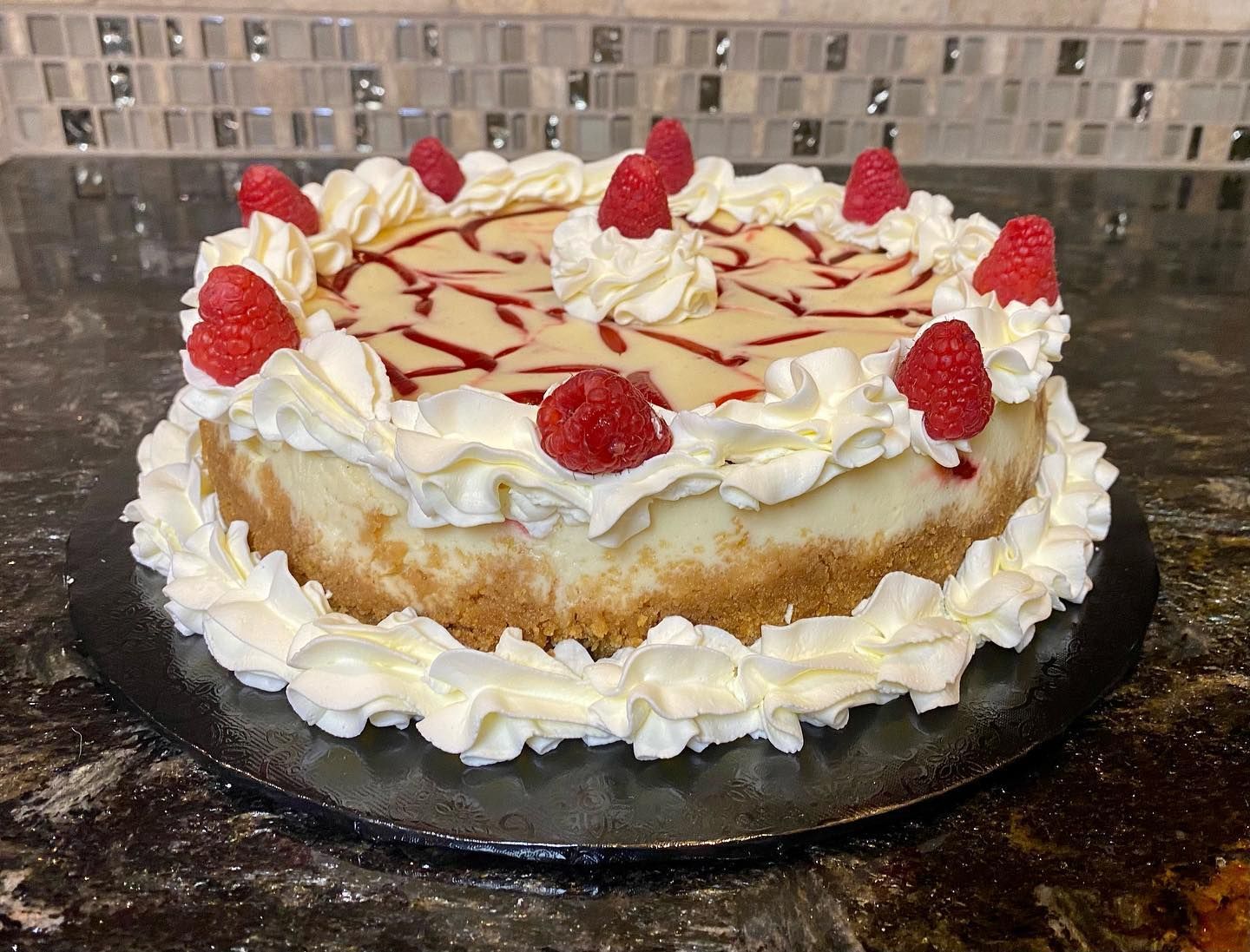 Vanilla cake with whipped cream, raspberries, and caramel drizzle on a black platter