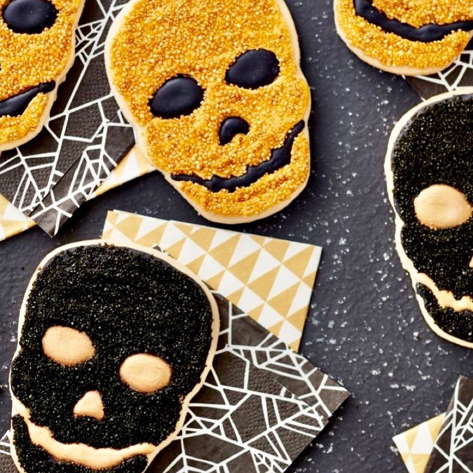 Skull-shaped cookies with black and gold icing on patterned napkins