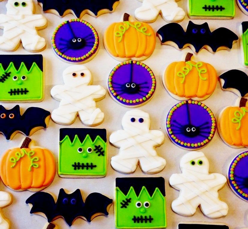 Assorted Halloween cookies with pumpkins, ghosts, bats, and Frankenstein faces in orange, purple, black, and green