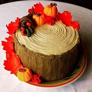 Round frosted cake decorated with small pumpkins and red autumn leaves on a plate