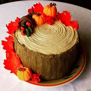 Round frosted cake decorated with small pumpkins and red autumn leaves on a plate