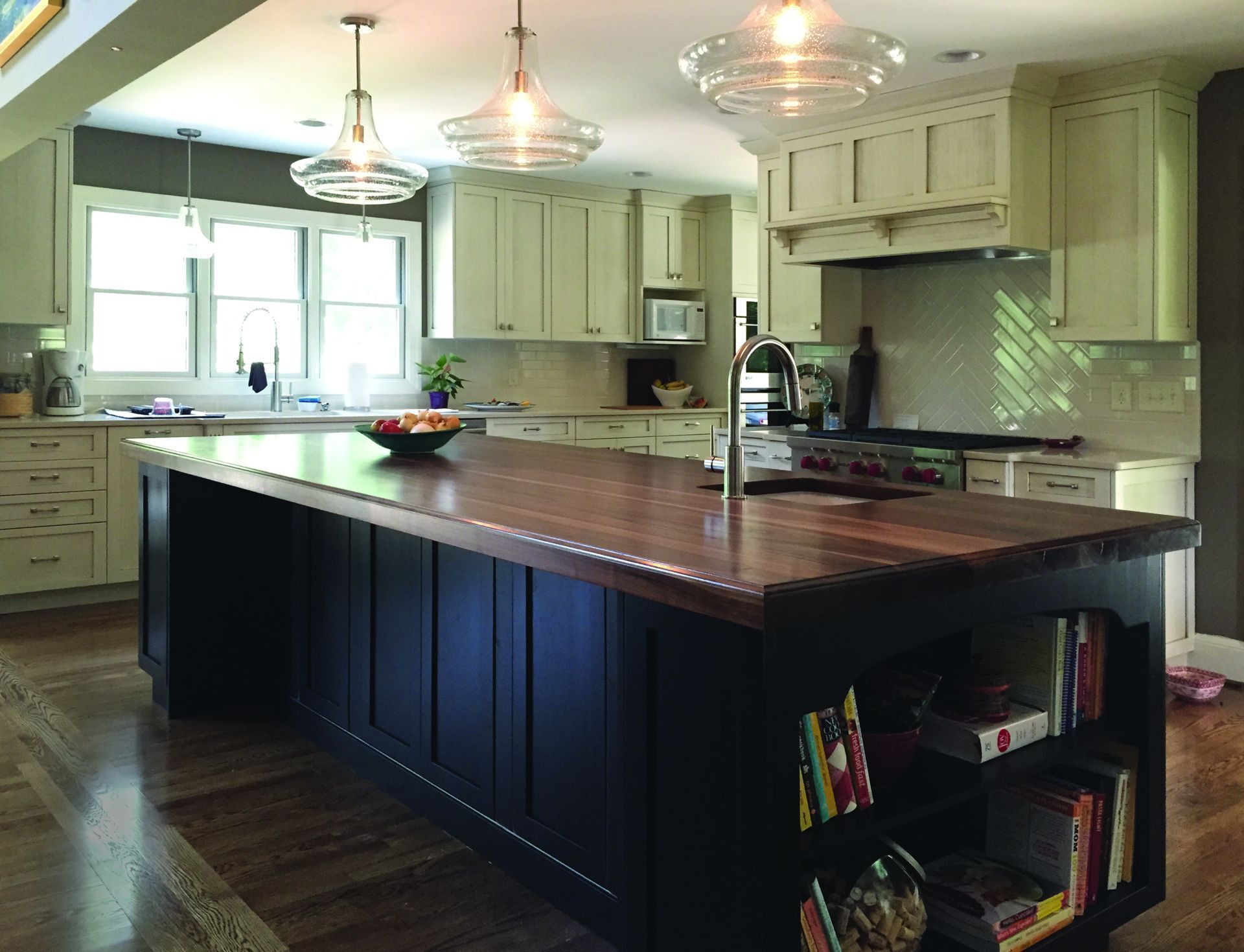 Modern kitchen with large dark walnut wood island, hanging lights, and white cabinets
