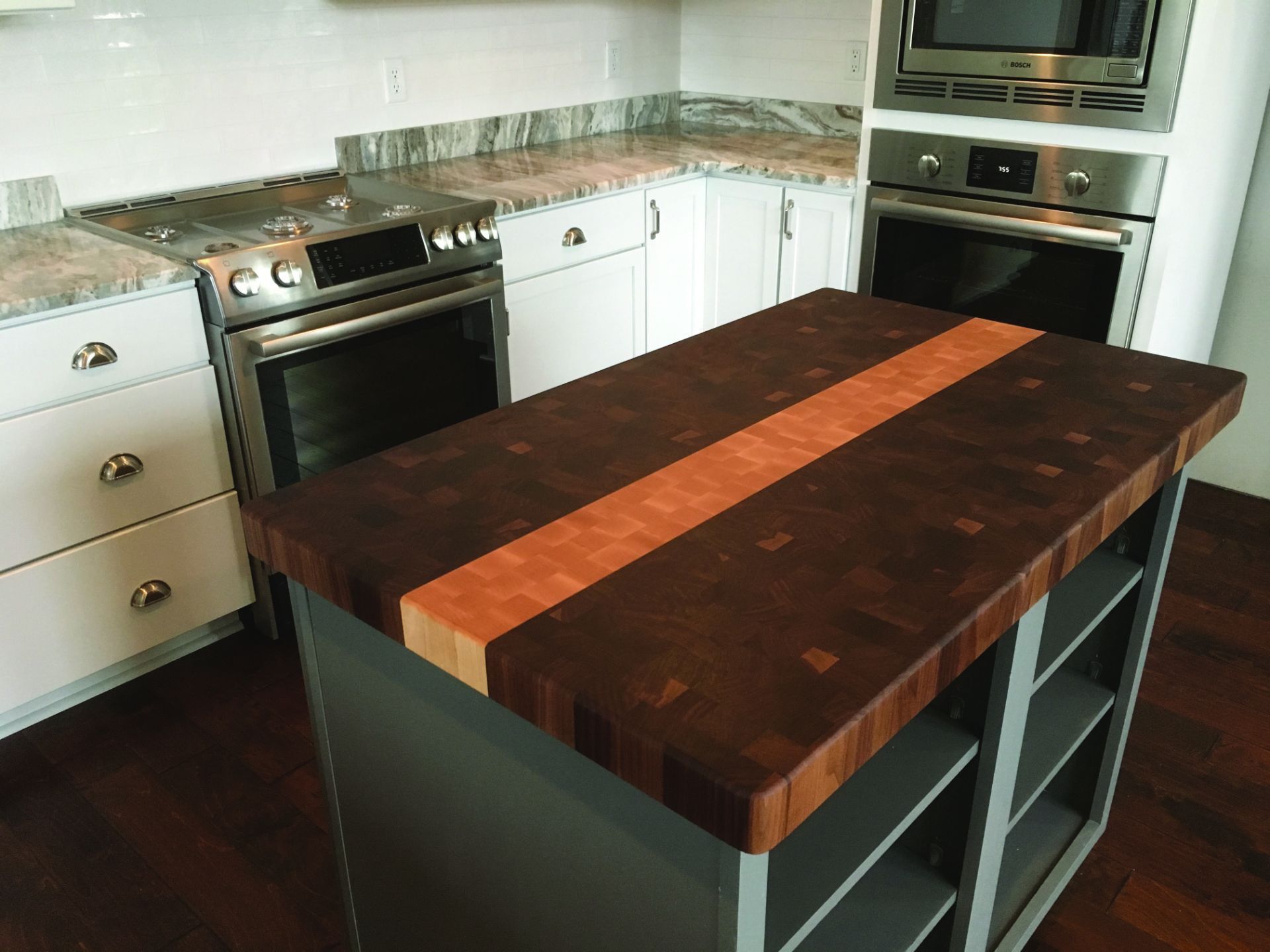 Kitchen island with butcher-block top in a white kitchen, beside a stove and built-in oven.