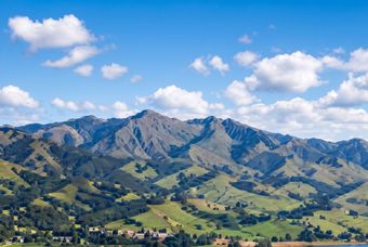 Mountain range above green valleys under a bright blue sky with scattered white clouds