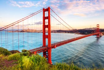 Golden Gate Bridge at sunset, with red towers spanning blue water under a pastel sky