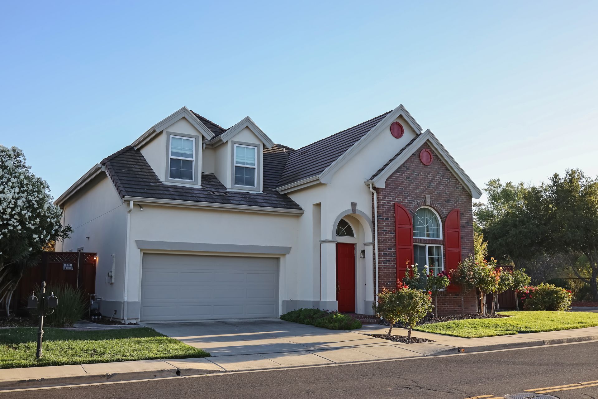 Suburban house with white garage, red front door, and brick and gray siding under a clear sky