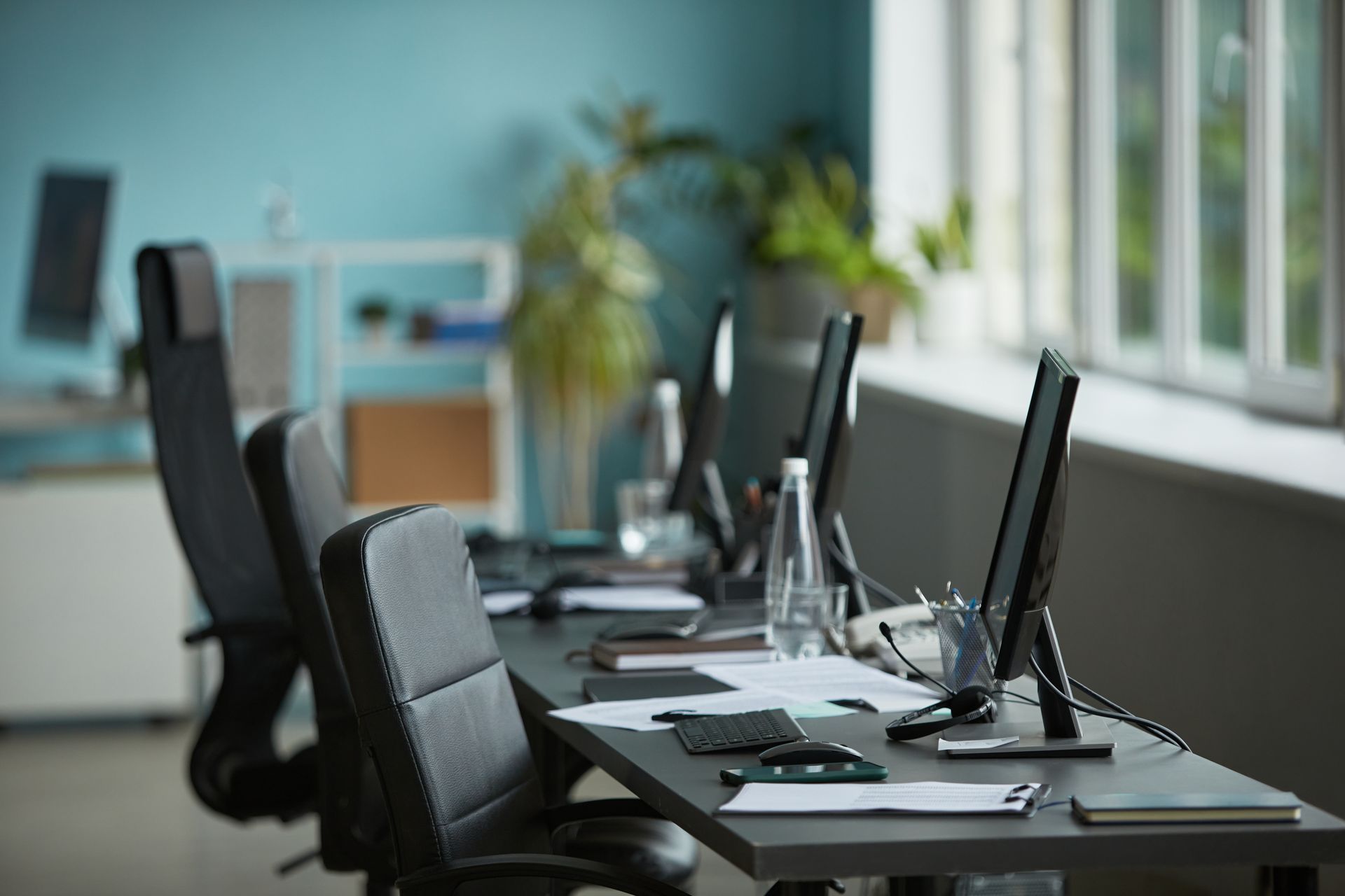 Empty office conference table with monitors, chairs, and papers by large windows