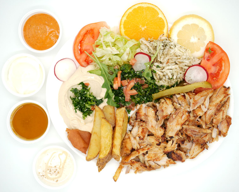 Shawarma platter with meat, hummus, salad, fries, sauces, and fruit.