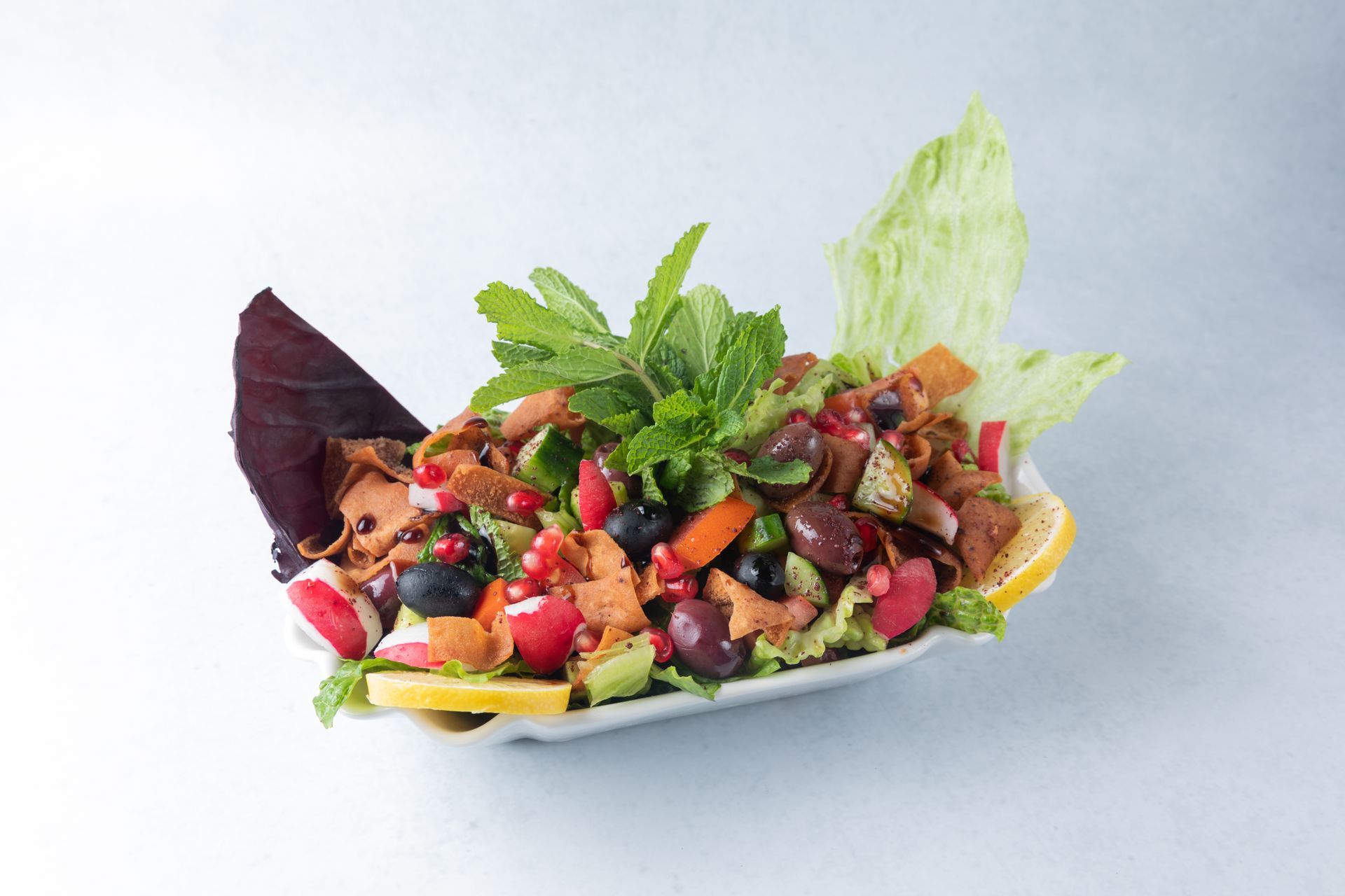 Lebanese fattoush salad in white dish with fresh herbs, bread, and colorful vegetables.