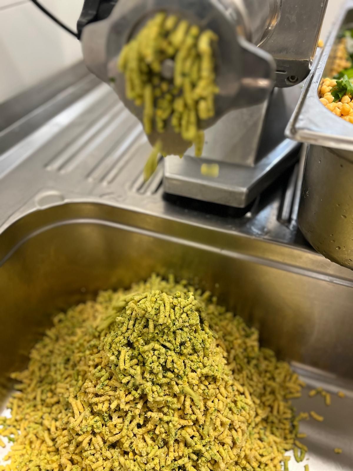 Green food being ground by a machine into a tray, close-up shot.