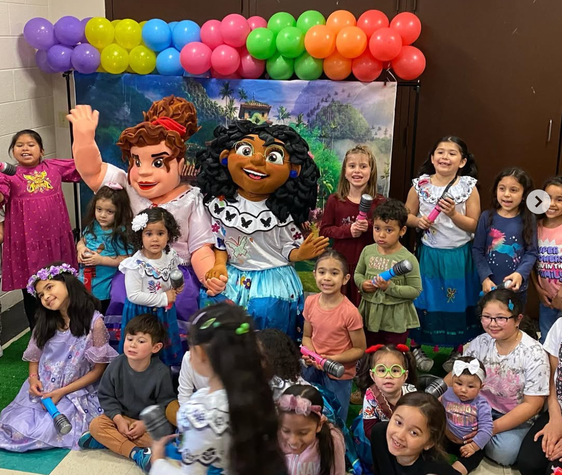 Children posing with mascots at a colorful birthday party with balloon arch backdrop