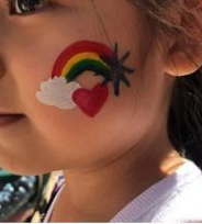 Child’s cheek with a rainbow, heart, cloud, and star face painting at a birthday party.