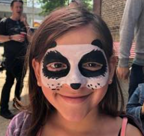 Girl with raccoon face paint smiling at a party.