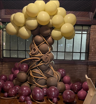 Balloon sculpture of a tree with gold canopy, brown trunk, at a party.