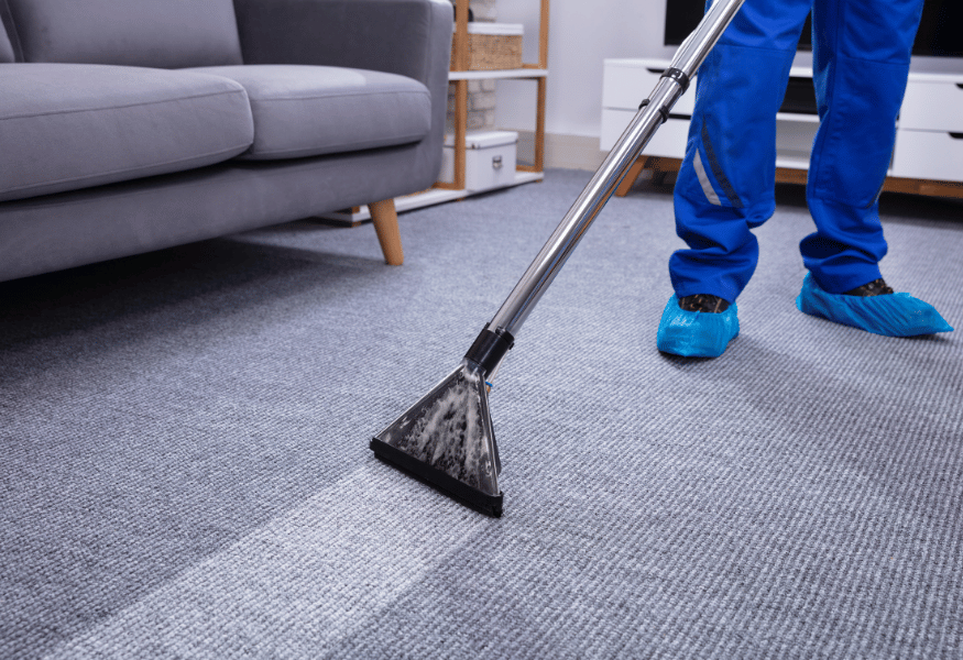 Person in blue cleaning carpet with a vacuum in a living room.