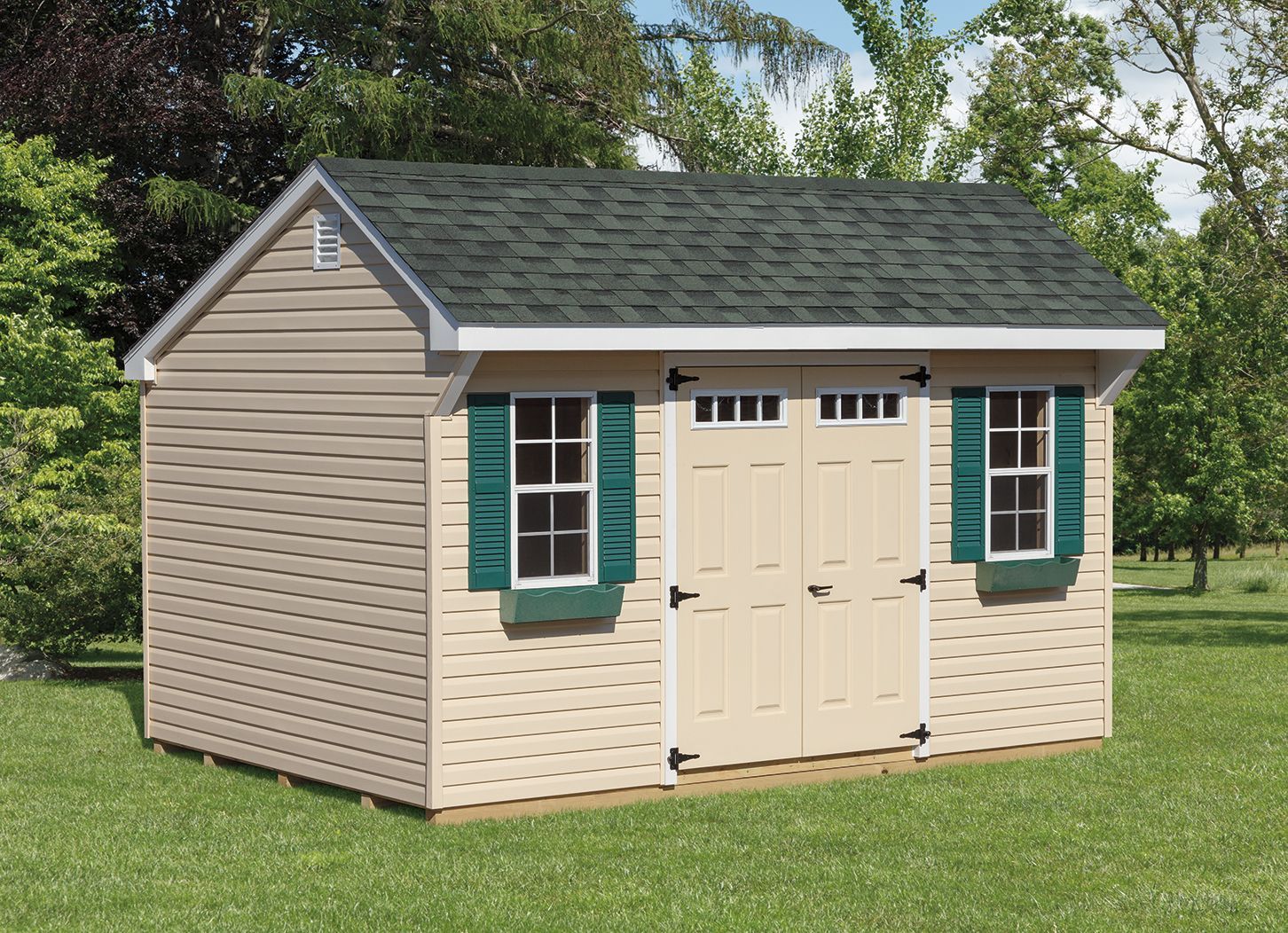 Tan storage shed with green shutters and roof on a grassy lawn.