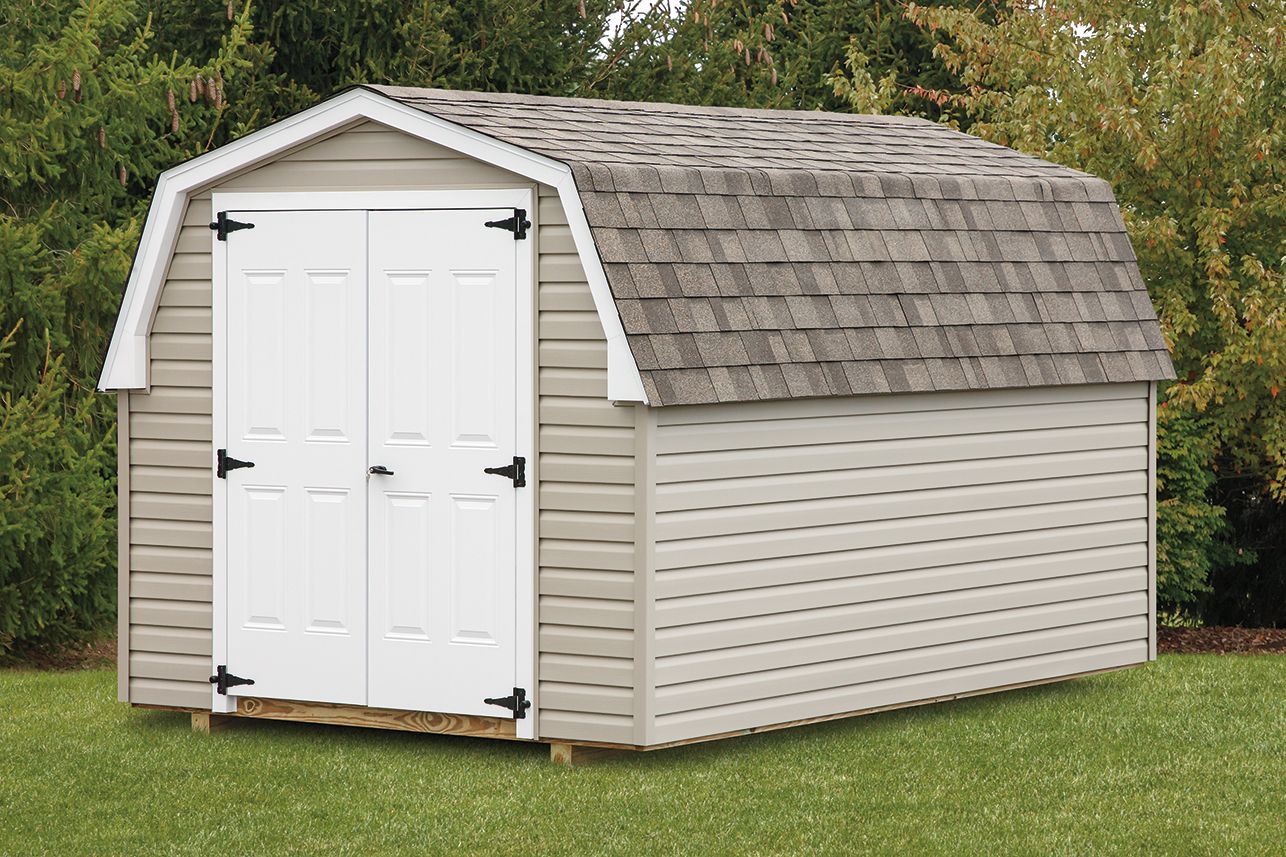 Tan-sided shed with white double doors, dark hinges, and a gray roof, standing on grass.