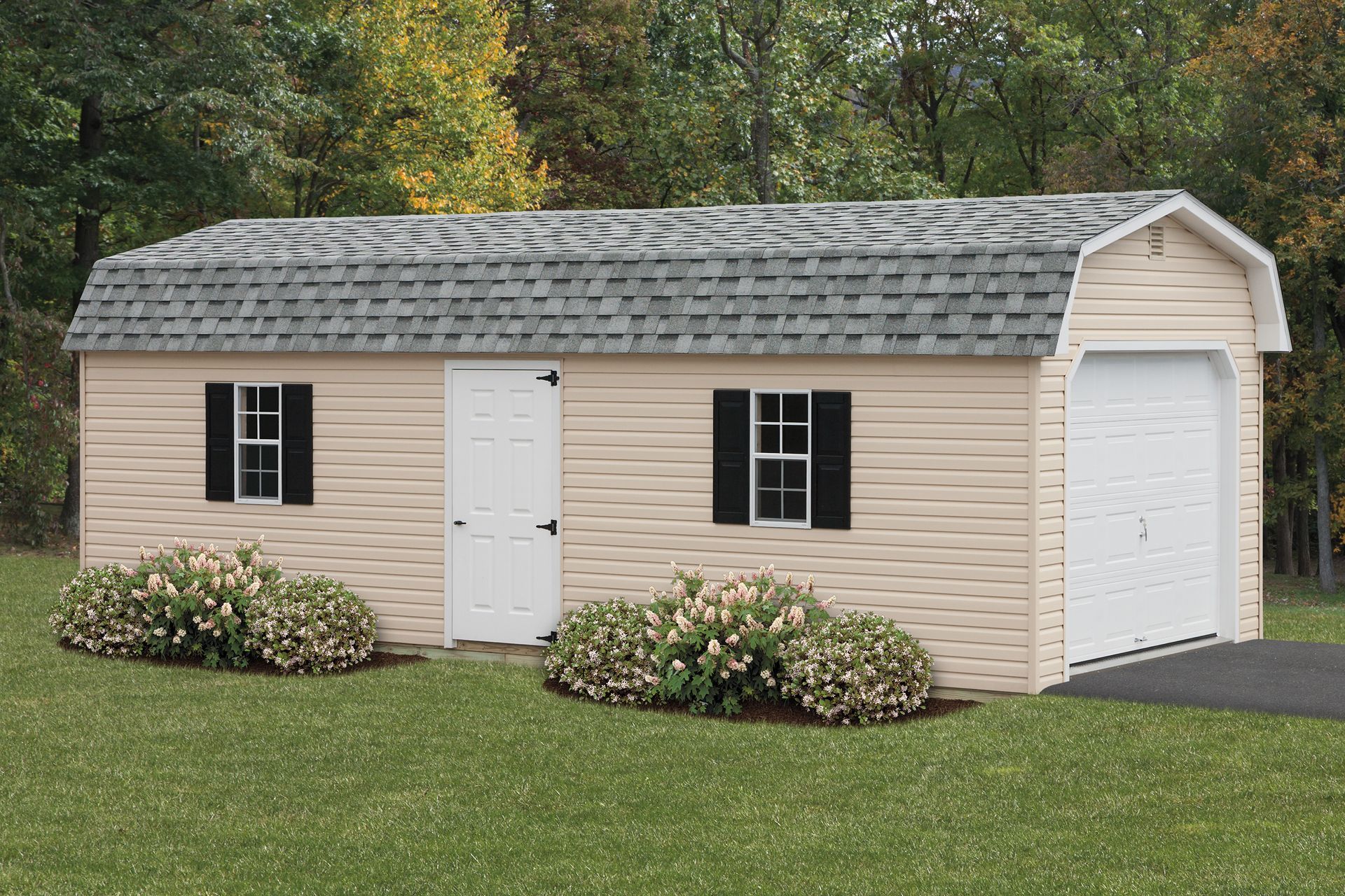 Tan barn-style shed with a grey roof, white door, windows with black shutters, and garage door on green grass.
