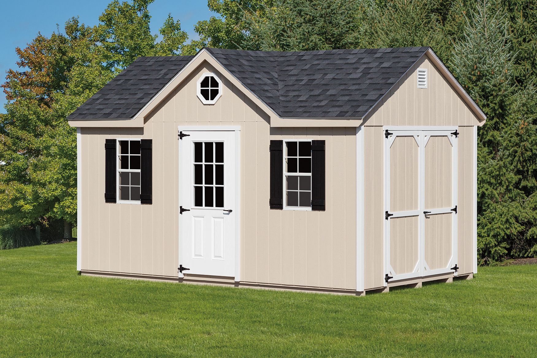 Tan shed with black roof, white trim, door, shutters, and an oval window, on a grassy lawn.