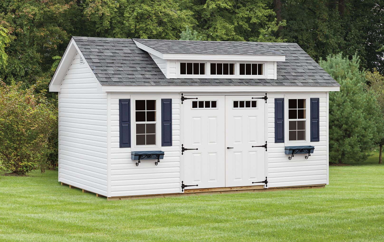 White storage shed with black shutters, windows, and decorative dormer, on a green lawn.