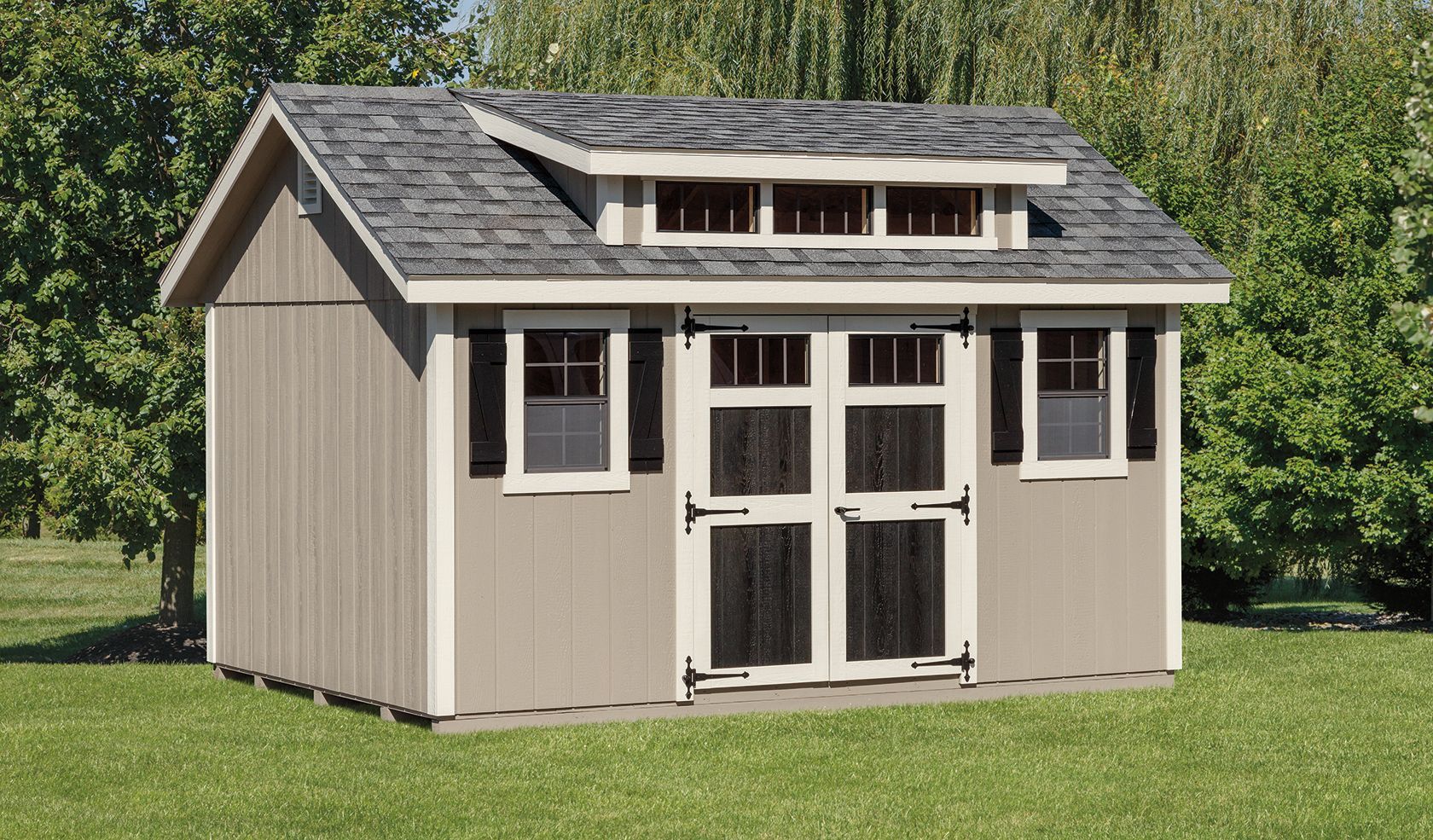 Tan shed with dark roof and trim, windows, and double doors, in a grassy yard.