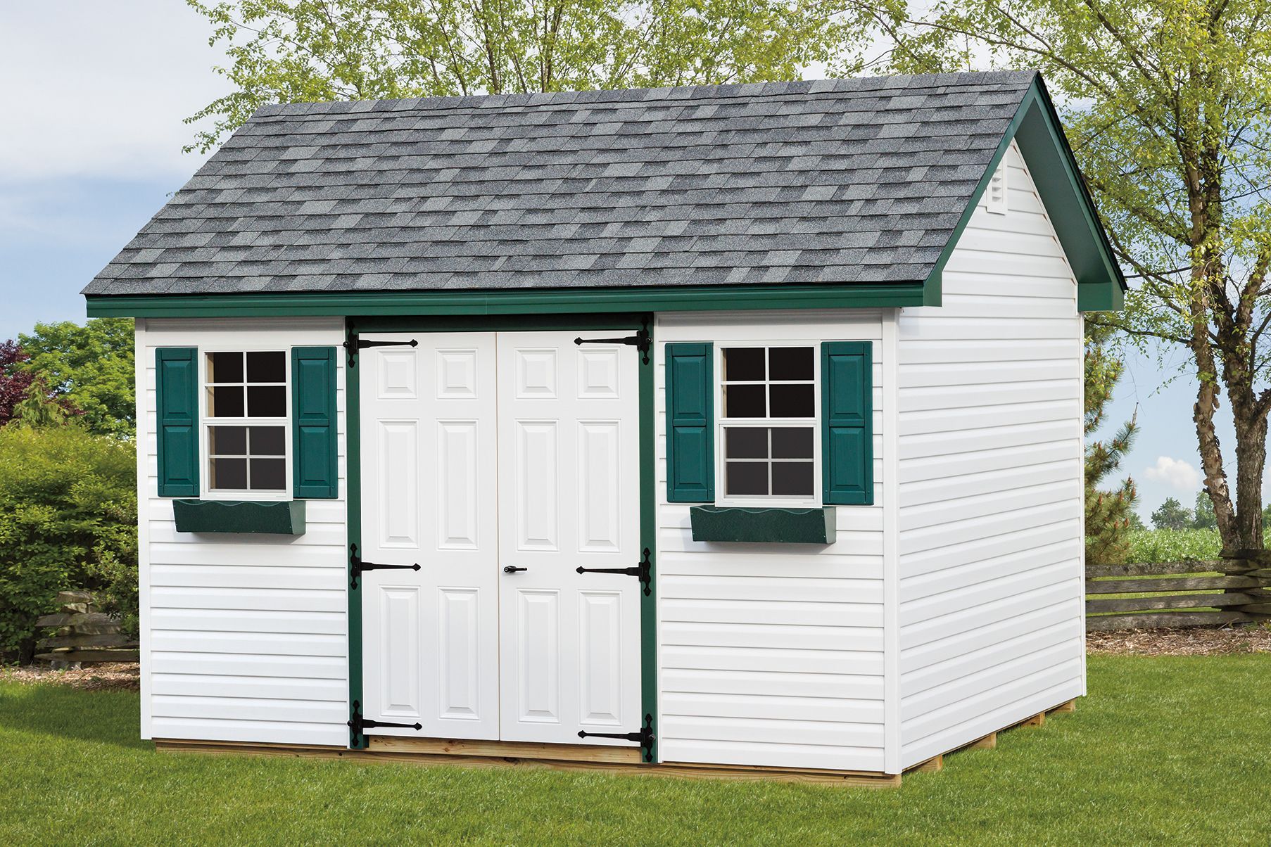White shed with green trim, gray roof, two windows with shutters, and double doors, set on a grassy lawn.
