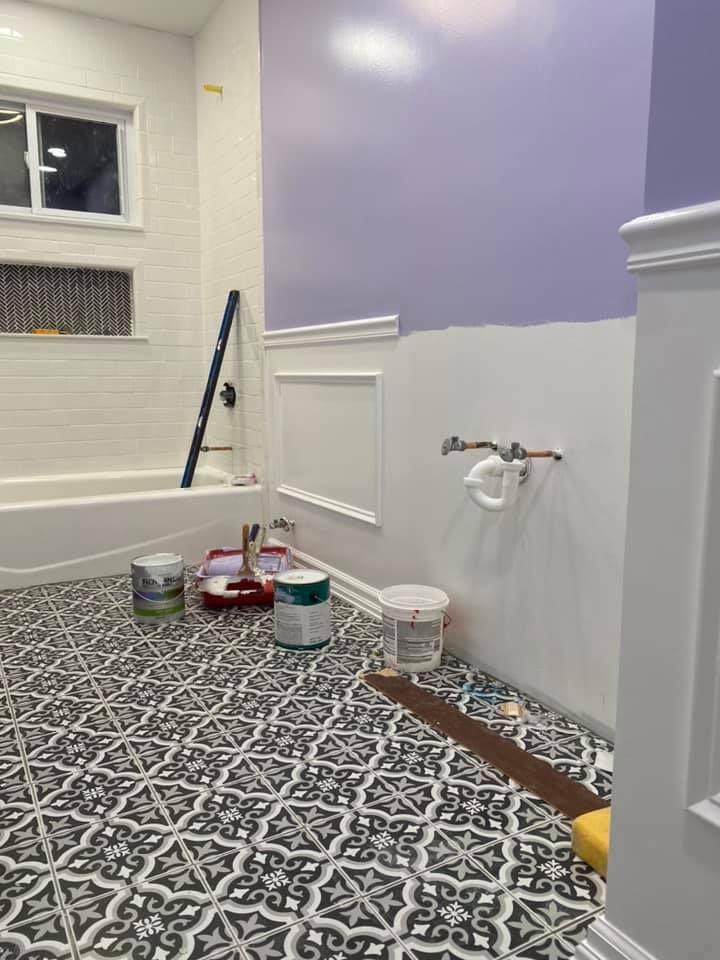 Painted bathroom under renovation with buckets, tools, patterned tile, and purple-and-white walls.